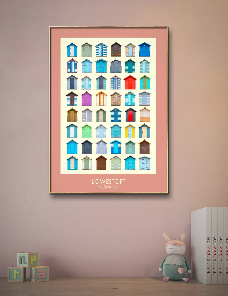 The Lowestoft print with a coral border in a gold frame on a dusky pink wall, above a shelf of children's books and toys