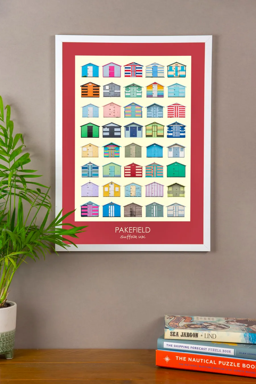 The Pakefield print with a spade red border in a white frame on a grey wall, above a stack of nautical books
