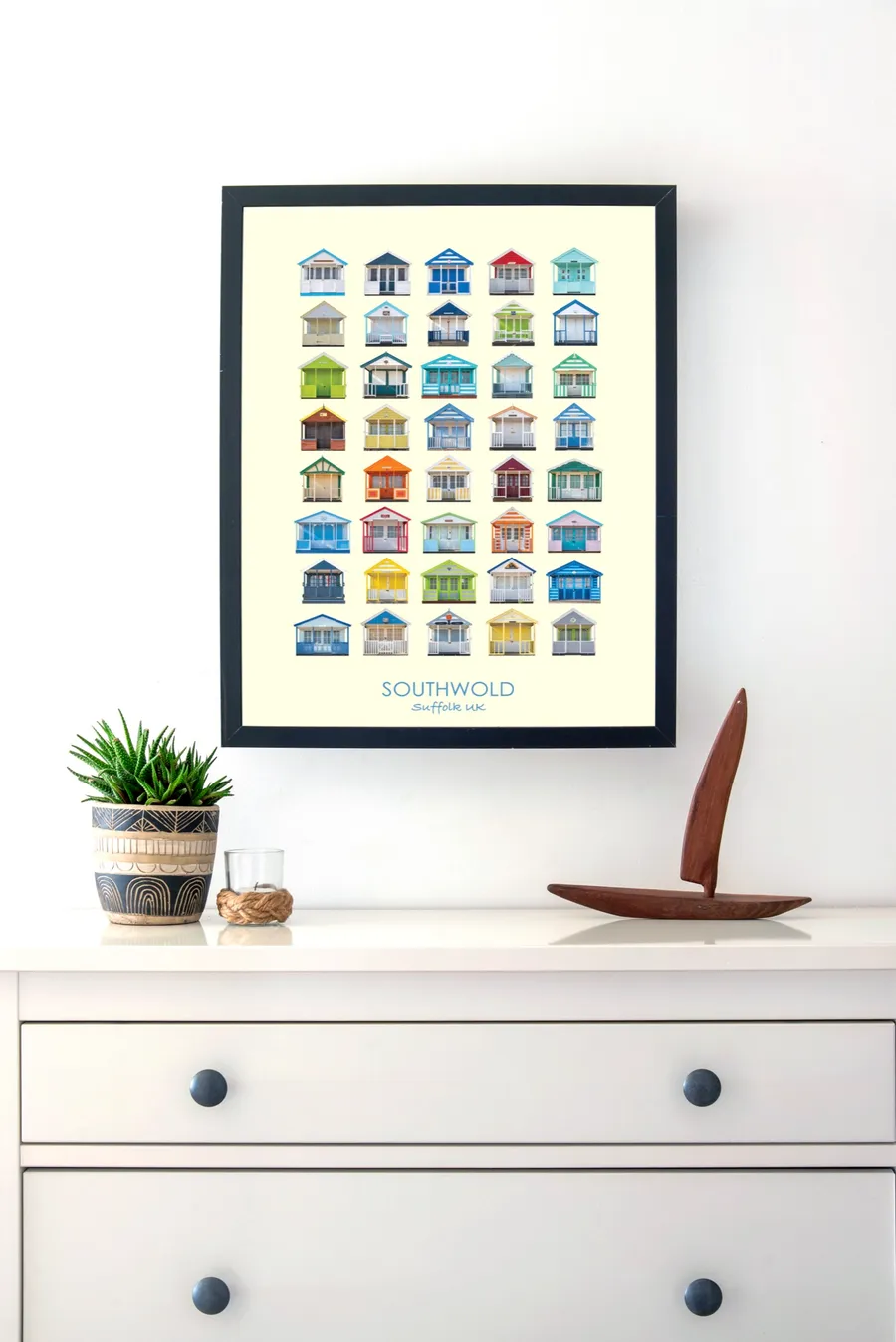 The Southwold print in a slim black frame on a white wall above a chest of drawers, beside a potted succulent and a small wooden sailing boat